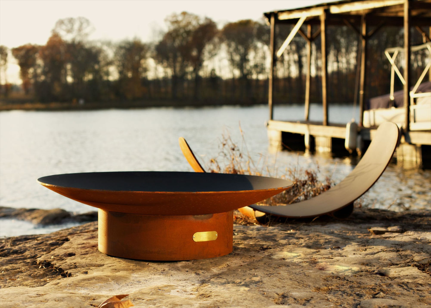 Asia Series oriental steel fire pit showcased on a lakeside rock at dusk.