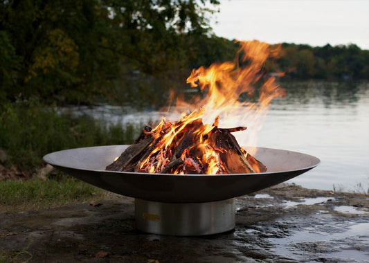 The Bella Vita Series Fire Pit, Displayed lakeside, with a huge burning flame.