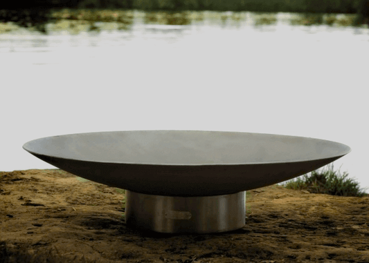 The Bella Vita Series Fire Pit, Displayed on the sandy beach of a lake.