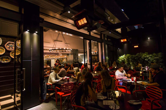 People dining at tables outside a restaurant at night, with the bromic gas patio heater giving off heat.