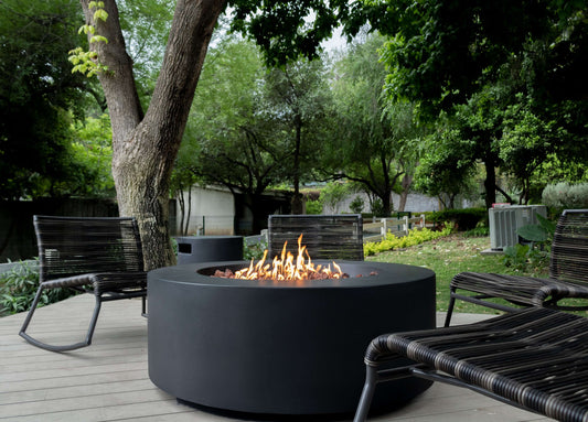 The Coliseo Concrete Cylinder Fire Pit 01 in the Noir Color option, displayed on a beautiful backyard patio with a warm flame.