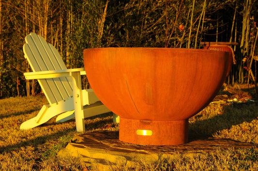 The Beautiful Crater Fire Bowl, showcasing its beautiful, and strong hand crafted design in a backyard, surrounded by chairs.