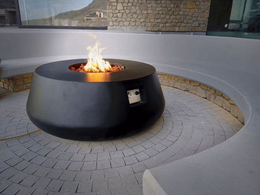 The Indiana Modern Fire Pit 01 in the Noir color option. Presented with a warm flame, on a outdoor patio.