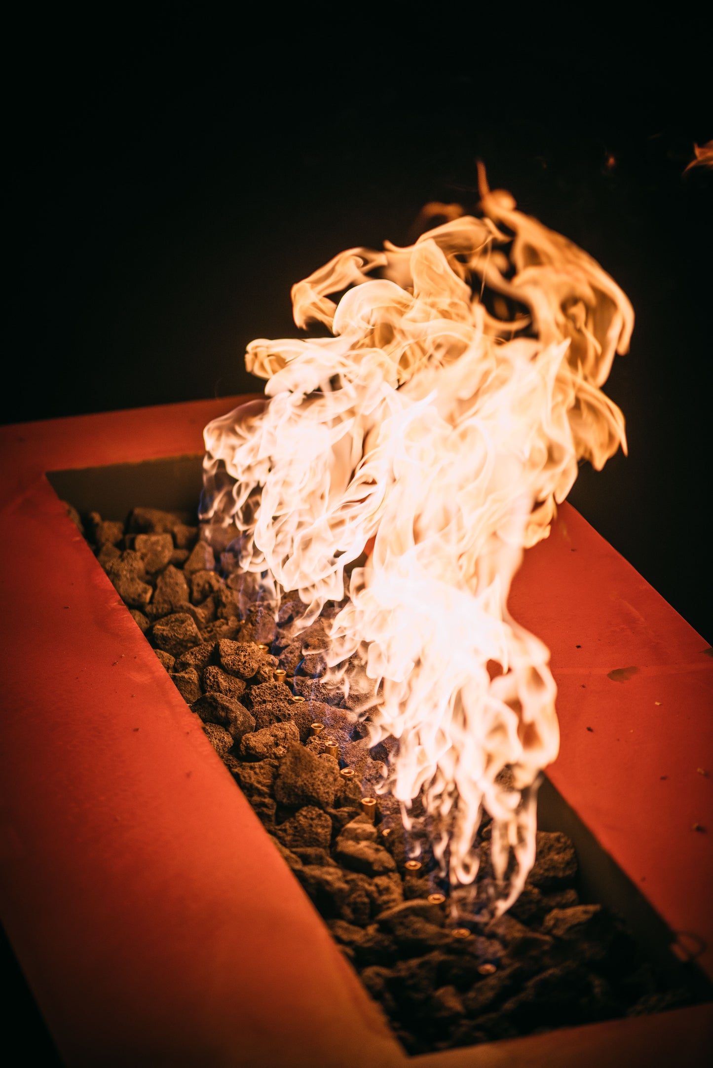 The hand crafted Linear Series Fire Pit, displayed on a cozy backyard patio with a warm flame.