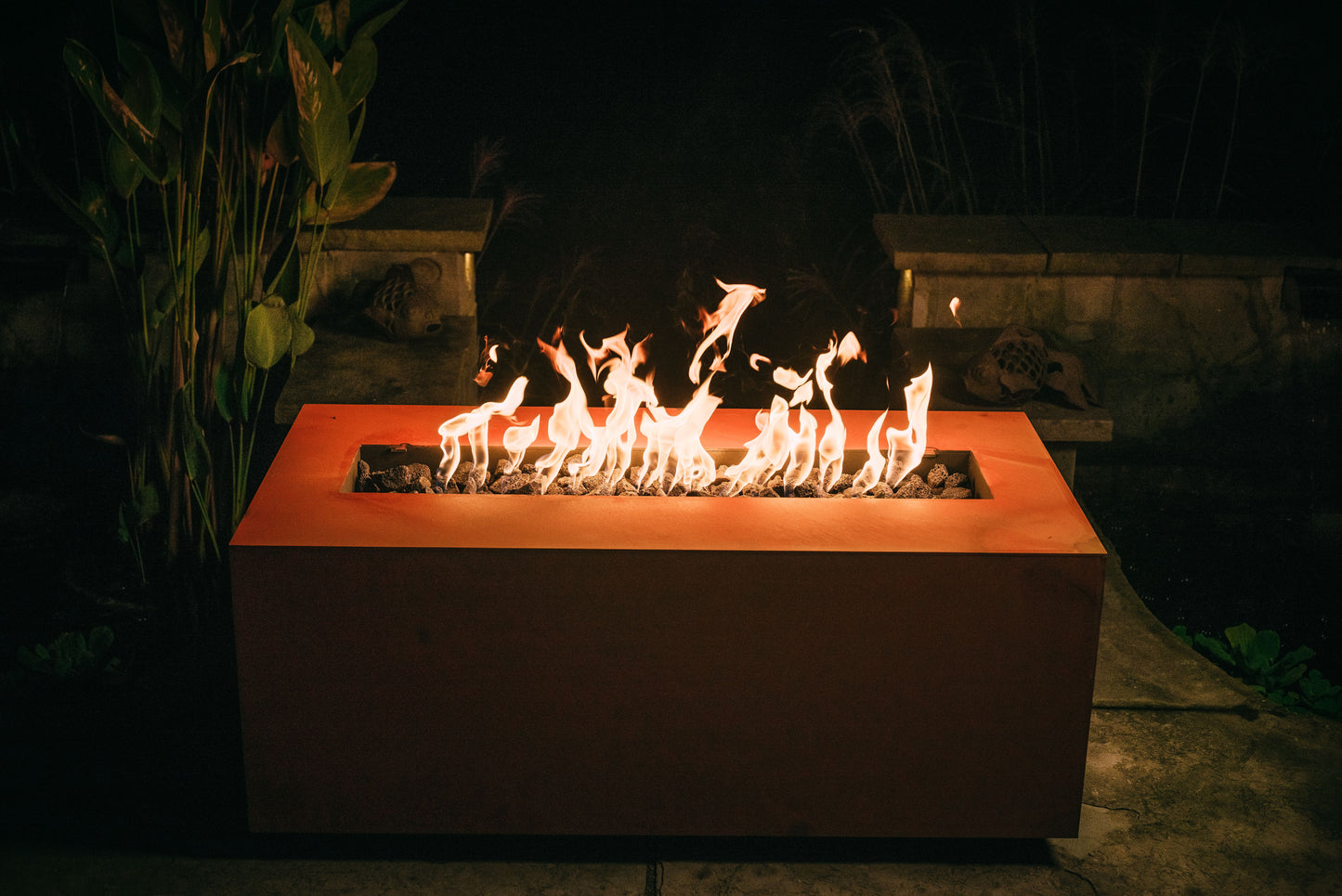 The hand crafted Linear Series Fire Pit, displayed on a cozy backyard patio with a warm flame.