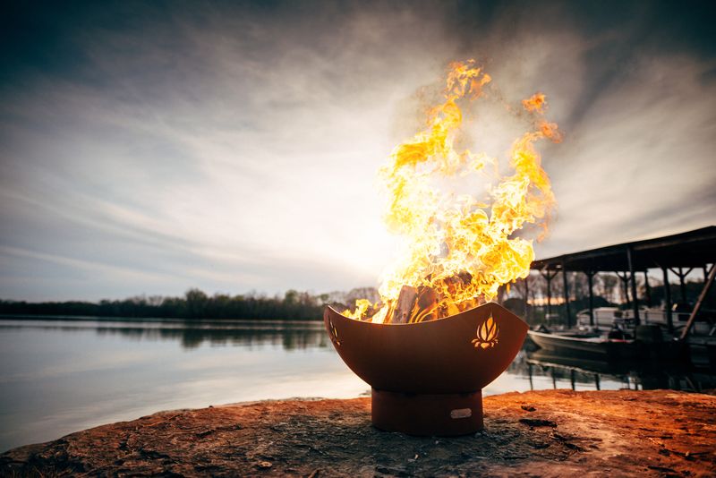 The gorgeous Namaste Fire Pit, Displayed on a lakeside rock, full of wood with a huge roaring flame.