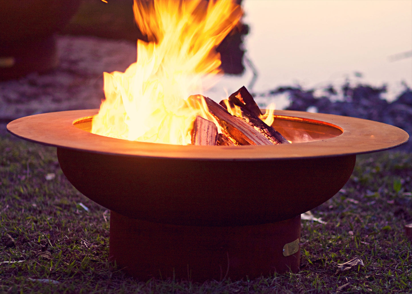The Handcrafted saturn fire pit displayed on a lakeside shore with a huge warm flame.