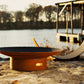 Asia Series oriental steel fire pit showcased on a lakeside rock at dusk.