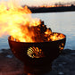 The BeachComber Fire Pit, displayed on the lake shore, burning firewood with a huge flame.