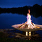 The Bella Vita Series Fire Pit, Displayed lakeside, with a huge burning flame at night.