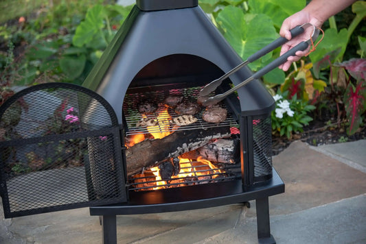 Black Wood Burning Outdoor Firehouse with Chimney & Cooking Grate being used to cook chicken and Steak.