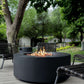 The Coliseo Concrete Cylinder Fire Pit 01 in the Noir Color option, displayed on a beautiful backyard patio with a warm flame.