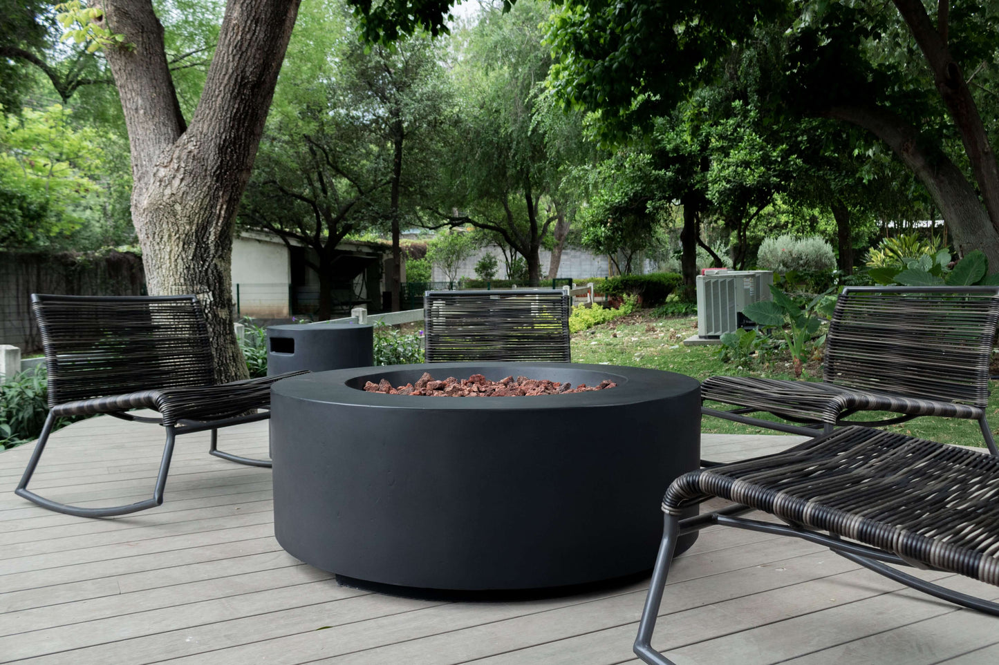 The Coliseo Concrete Cylinder Fire Pit 01 in the Noir Color option, displayed on a beautiful backyard patio.