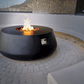 The Indiana Modern Fire Pit 01 in the Noir color option. Presented with a warm flame, on a outdoor patio.
