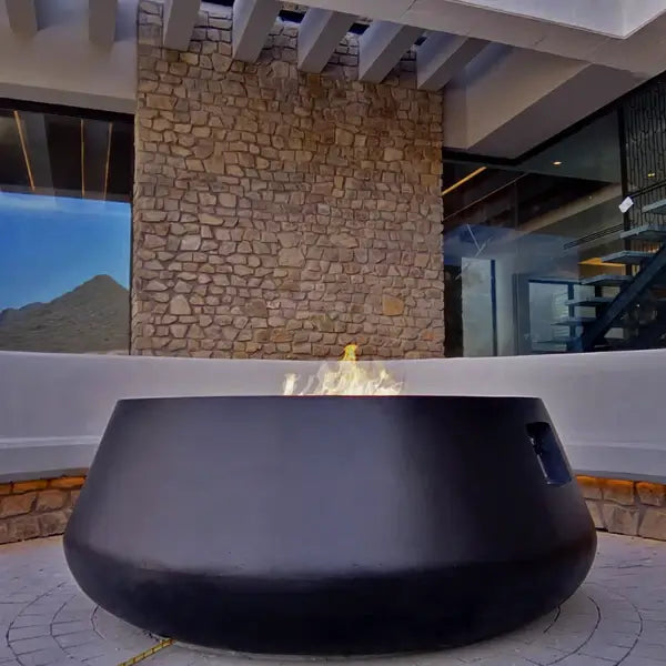 The Indiana Modern Fire Pit 03 in the Noir color option, displayed on a patio, with a warm roaring flame.