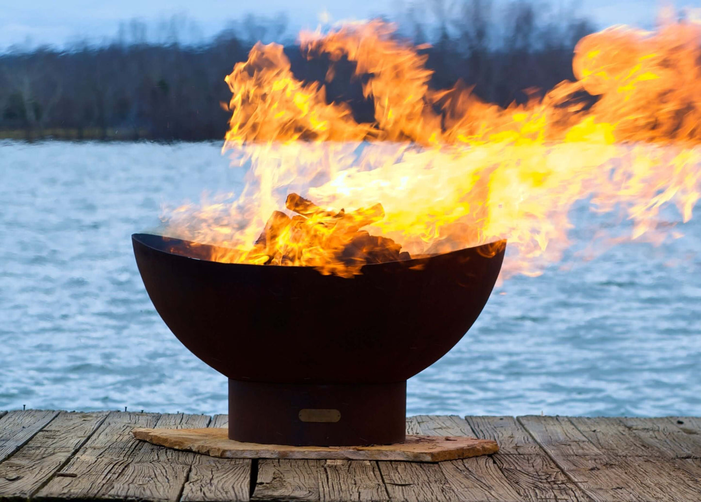 The Beautiful Scallop Fire Pit, displayed on a lakeside dock, with huge warm flame.