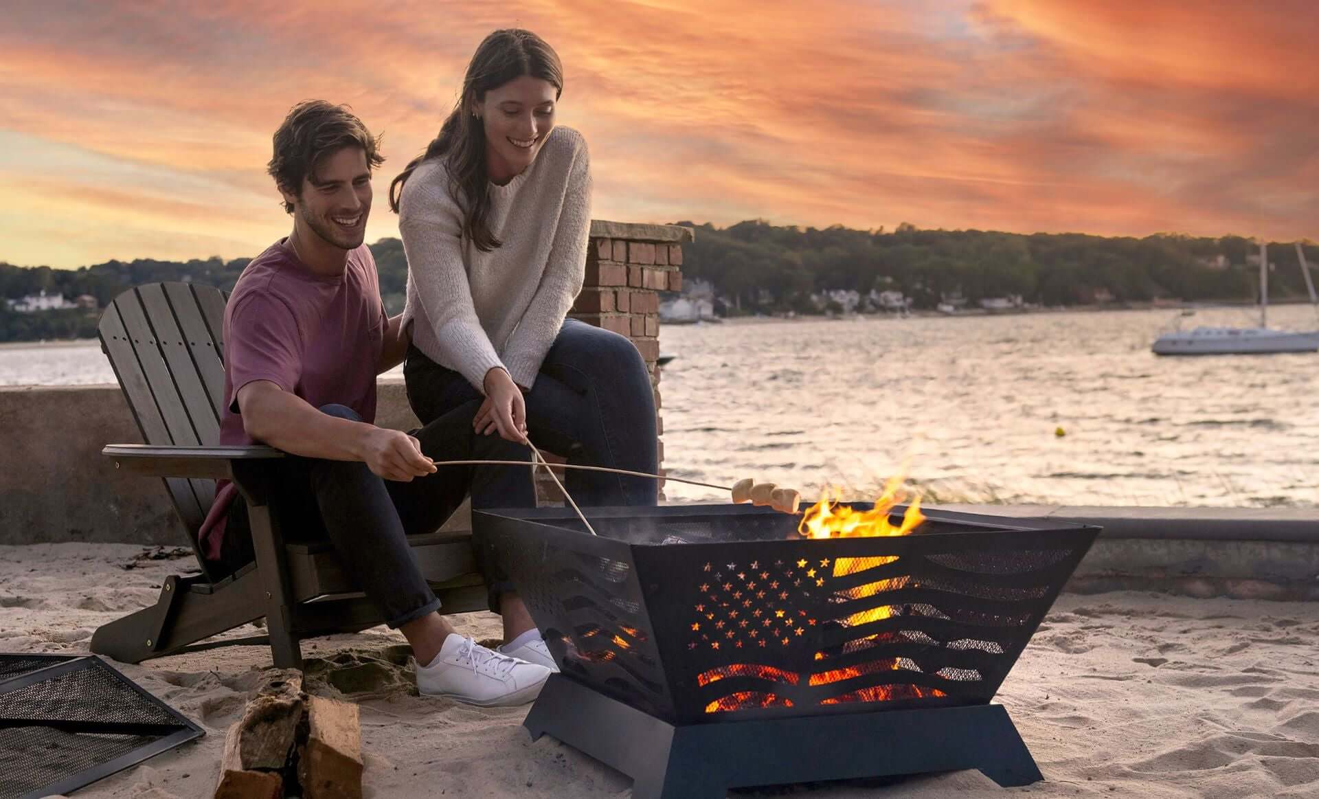  The Patriot Wood Burning Fire Pit on  a oceanside beach, with two people roasting marshmallows.