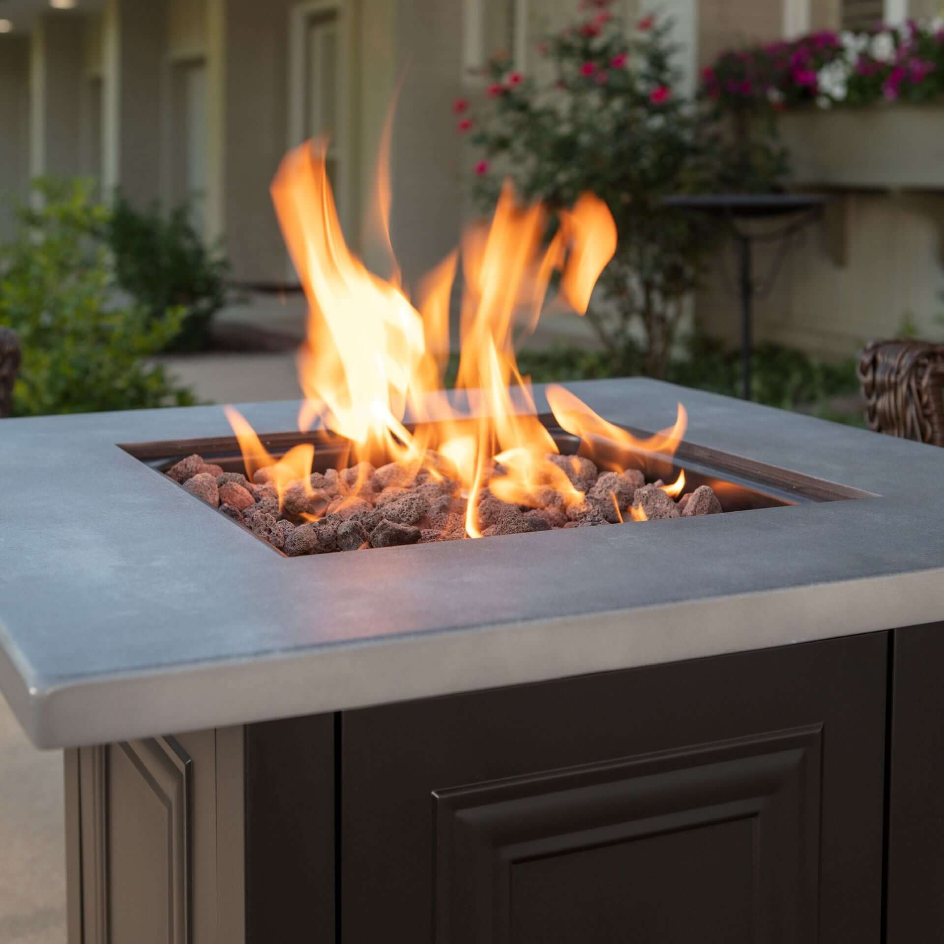 The Wakefield, LP Gas Outdoor Fire Pit with Concrete Resin Mantel displayed on a backyard patio, featuring a warm roaring flame.